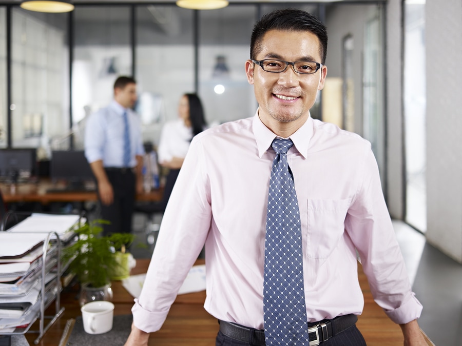 Asian Businessman Standing In Office Arms Crossed With Multinati